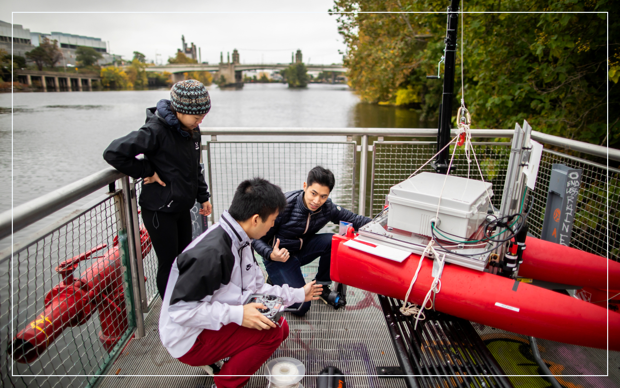 Three people calibrating remote equipment in an enclosed pier over a river