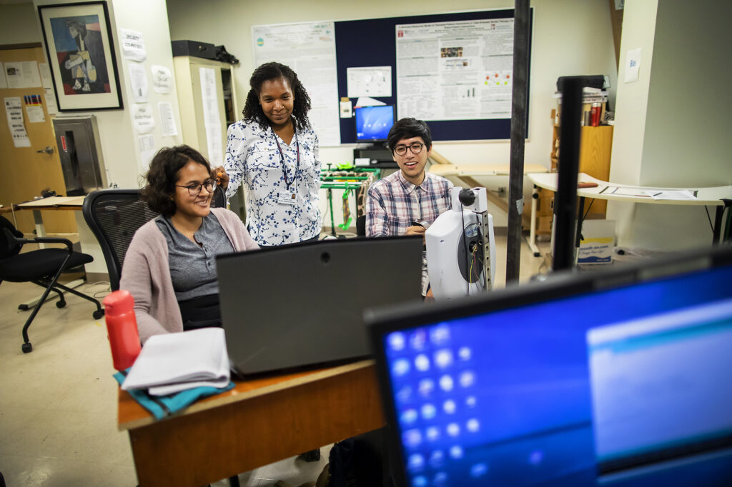 Three researchers huddle around a computer to analyze data
