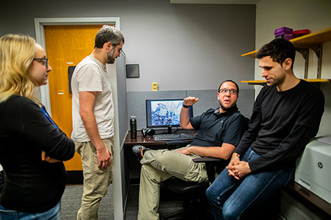 Four people sitting in a small office with a computer